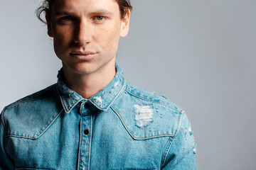 Portrait of a handsome long-haired man with drawn hair and freckles dressed in a denim shirt
