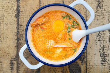 Ramen with spicy soup and prawn in blue bowl on wooden table.