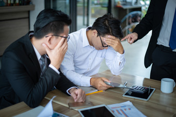 boss is very angry and shouted to employee for reported sales decrease, employee is stressed and put hands on his head.