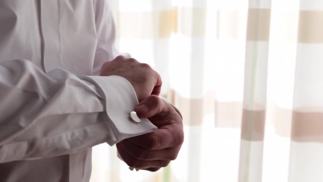 Man adjusting cufflink in front of window light