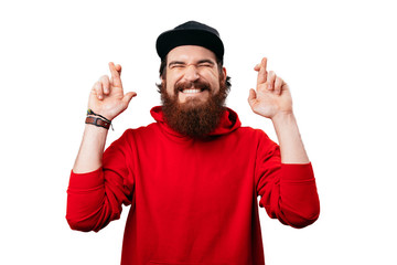 Photo of excited bearded man in red hoody crossing his fingers for more luck
