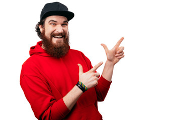 Happy smiling bearded guy  in red hoody, pointing with fingeres away over white background