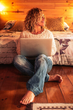 People using technology at home - happy beautiful caucasian woman with laptop on the legs sitting in the bedroom - home or hotel place and warm sweet lights