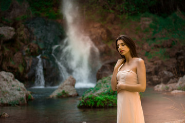 Fototapeta na wymiar Sexy woman posing on the rock among green tropical plants and beside beautiful waterfall with blue water. Fairy tale.