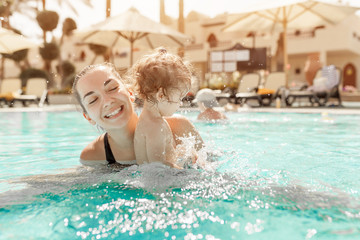 Mom and little daughter are played in the open swimming pool. Family with one child on vacation in...