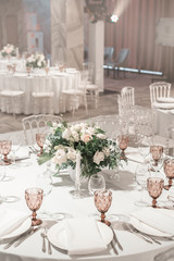 Flower arrangement in the center of the table. Interior of restaurant for wedding dinner, ready for guests. Round Banquet table served. Catering concept.