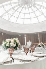 Flower arrangement in the center of the table. Interior of restaurant for wedding dinner, ready for guests. Round Banquet table served. Catering concept.