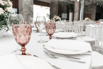 Wine glasses on round Banquet table served. Interior of restaurant for wedding dinner, ready for guests. Decorated with floral arrangement. Dishes, wine glasses and napkins. Catering concept.