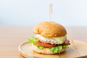 Chicken burger with cheese,lettuce and tomato in wooden dish.