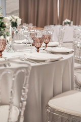 Wine glasses on round Banquet table served. Interior of restaurant for wedding dinner, ready for guests. Decorated with floral arrangement. Dishes, wine glasses and napkins. Catering concept.