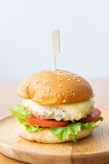 Chicken burger with cheese,lettuce and tomato in wooden dish.