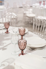 Wine glasses on round Banquet table served. Interior of restaurant for wedding dinner, ready for guests. Decorated with floral arrangement. Dishes, wine glasses and napkins. Catering concept.