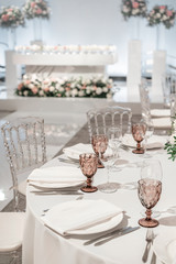 Wine glasses on round Banquet table served. Interior of restaurant for wedding dinner, ready for guests. Decorated with floral arrangement. Dishes, wine glasses and napkins. Catering concept.