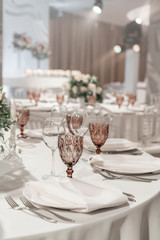 Wine glasses on round Banquet table served. Interior of restaurant for wedding dinner, ready for guests. Decorated with floral arrangement. Dishes, wine glasses and napkins. Catering concept.