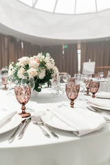 Wine glasses on round Banquet table served. Interior of restaurant for wedding dinner, ready for guests. Decorated with floral arrangement. Dishes, wine glasses and napkins. Catering concept.