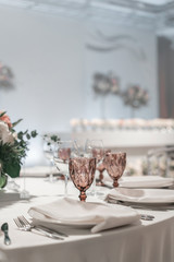 Glasses of wine on round Banquet table served. Interior of restaurant for wedding dinner, ready for guests. Decorated with floral arrangement. Dishes, wine glasses and napkins. Catering concept.