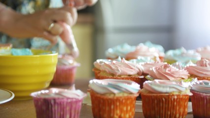 Decorating cup-cake with cream. Using cooking bag, confectioner making multicolor cupcakes for party. Shot of woman's hands putting butter cream on the tasty cakes, home bakery concept