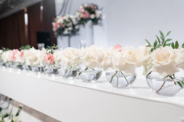 Small flower arrangements in ball glass vases. The table of the newlyweds. Interior of restaurant for wedding dinner, ready for guests. Catering concept.