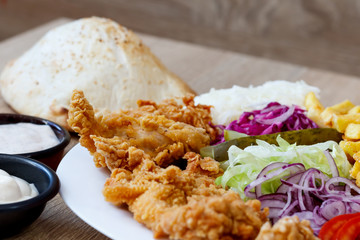 Chicken wings on the plate with bread, sauce, french fries, tomatoes, onion, pickles and cabbage salad on a wooden background.