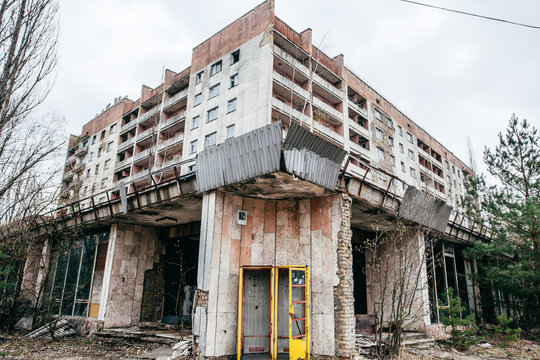 Telephone booth in a building with broken windows, shabby entrance in marble, with overgrown trees and grass in abandoned town of Pripyat after Chernobyl nuclear disaster