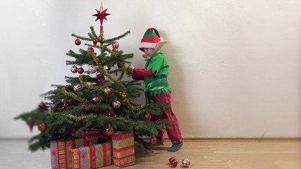 Funny elf arrange ornaments in Christmas tree, happy child waiting Christmas
