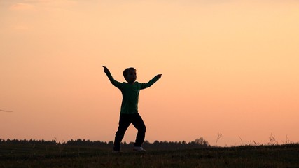 Happy child silhouette playing, singing, dancing, moving hands close sunset colorful sky, symbol of joyful childhood, concept of freedom, gorgeous nature