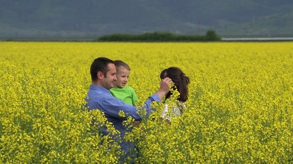 Fototapeta premium Father hold son in his arms arrange a flower in mother hair, blossom rape field