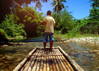 Man using pole to sail the bamboo raft in the river. One of career for tourism at Chiang Mai province in Thailand.Jungle and mountains with blue sky as background.