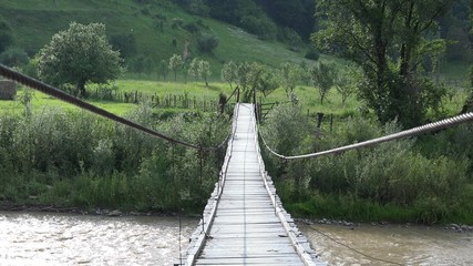 Suspension flyer rustic wooden bridge over mountain river, idyllic green nature