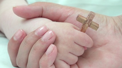 Detail of mother hand holding baby hand with christian cross, early education, real values to guide...