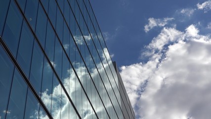 Fototapeta na wymiar Fluffy white clouds on blue sky mirrored in modern glass building