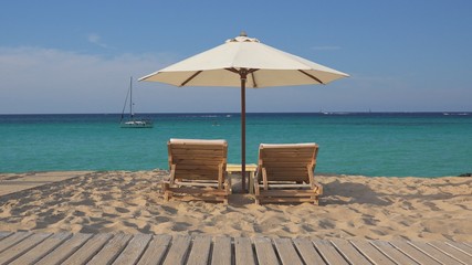 Tropical exotic beach with two empty wooden lounge sunbeds and big white umbrella, fine white sand and turquoise sea water, perfect relax in holiday luxury destination