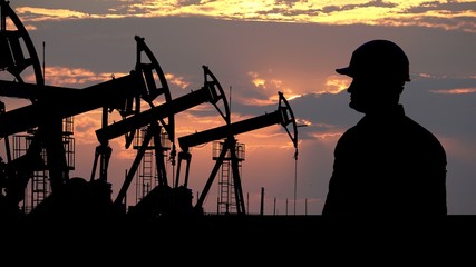 Engineer silhouette in front of oil pumps, red clouds sunset in background