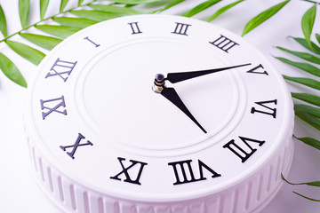 Beautiful white clock with leaves of tropical palm. The concept of time. holiday decoration images