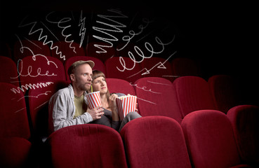 Obraz premium Young cute couple sitting in cinema, and eating popcorn while watching movie with doodle graphics
