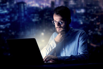 Young handsome businessman working late at night in the office with blue lights in the background