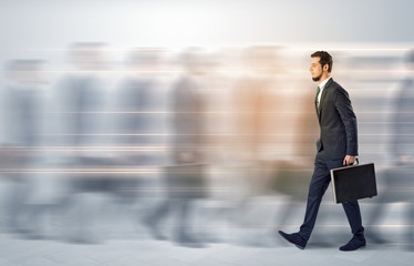Obraz premium Young businessman with briefcase hurry up on a crowded street with blurred people around 