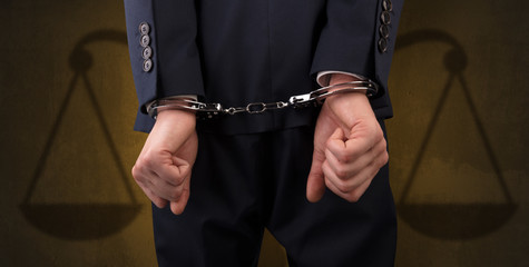 Arrested businessman in handcuffs with hands behind back and justice symbol wallpaper

