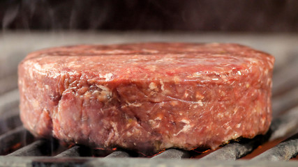 A large raw meat patty is grilled for a burger