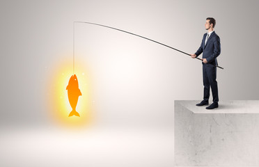 Young businessman fishing golden fish from the top of a building
