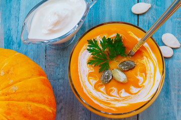 home made pumpkin cream soup with pumpkins and parsley leaves on blue wooden table. Vegetarian autumn pumpkin cream soup top view. pumpkin soup with sour cream and pumpkin seeds in a glass bowl.