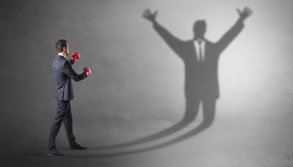 Businessman with boxing gloves fighting with disarmed businessman shadow
