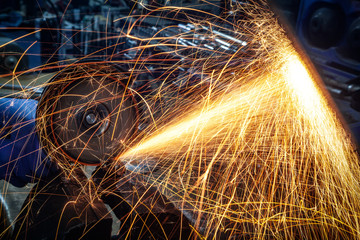 Close-up of a man sawing   bearing metal brake disk with a hand circular saw, bright flashes flying in different directions, in the background tools for an auto repair shop. Work of auto mechanics.