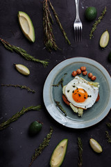 Top view of healthy breakfast scrambled eggs with bread and nuts in a plate on black background with avocado, rosemary, lime. Top view. Flat lay