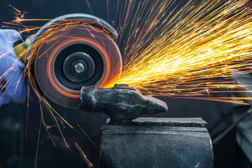 Close-up on the sides fly bright sparks from the angle grinder machine. A young male welder in a...