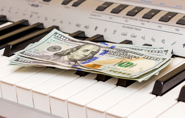 US Dollars lie on the piano keys. Payment for the concert, profit from performing musical works_