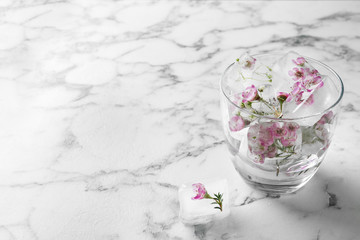 Glass of water with floral ice cubes on table. Space for text
