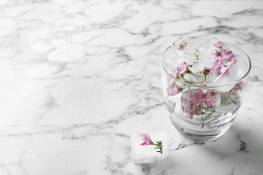 Glass of water with floral ice cubes on table. Space for text © New Africa
