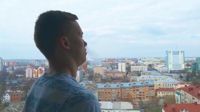 A young Asian man looks out over the city. Portrait of a handsome young man, amid the heights of the city. Close-up face of a young cool trendy man hovering a vape