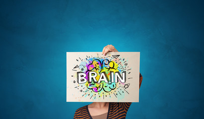 Young person holding white paper in front of her head with colorful brain concept
